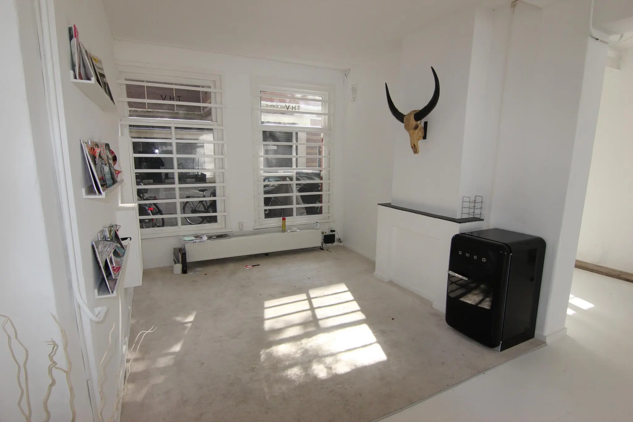 Woonkamer aan de Graaf Florisstraat met witte muren, grote ramen, een zwarte SMEG-koelkast en een stierenhoofd aan de muur.